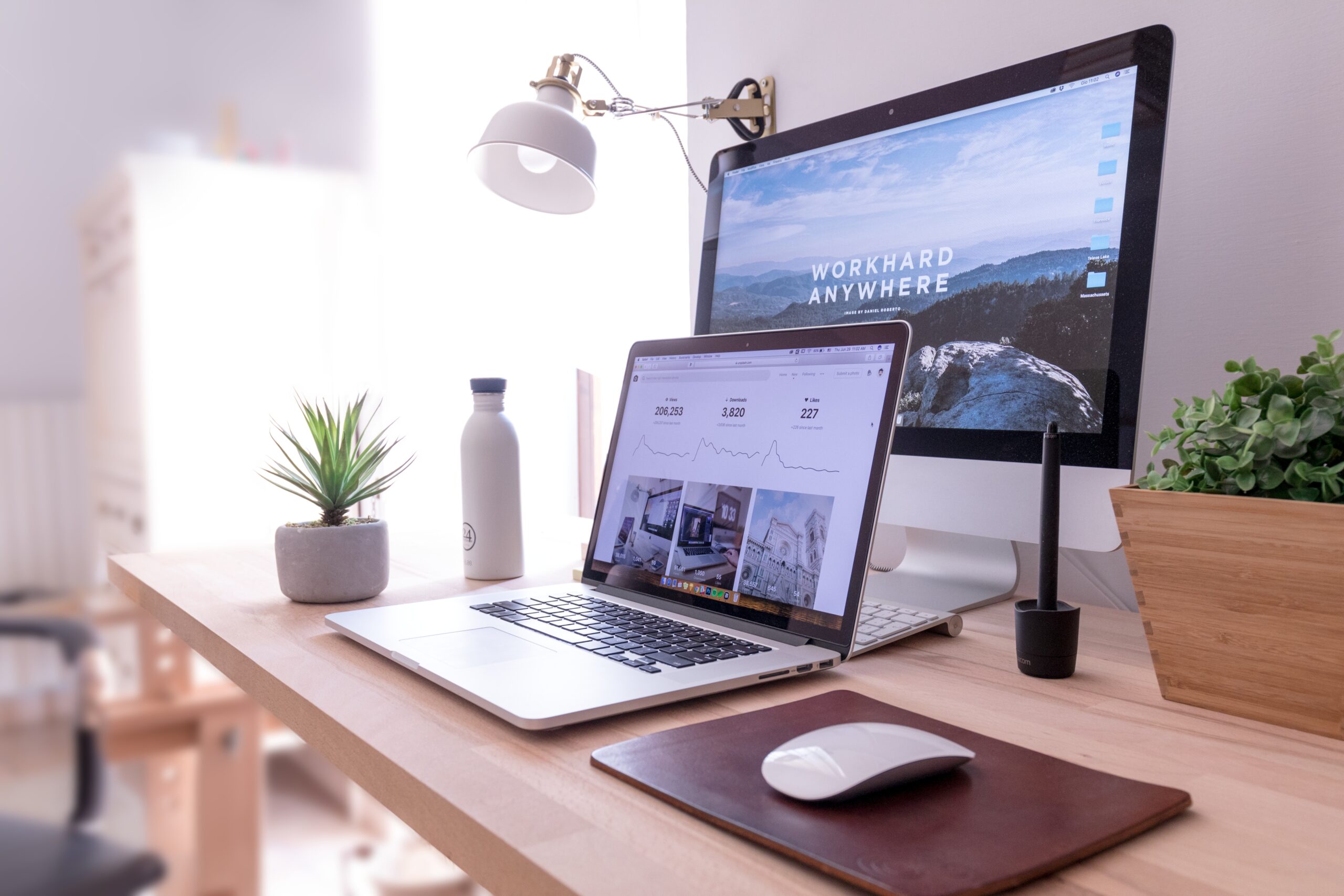 Desk with an Apple Mac, open laptop, mouse and plant pot